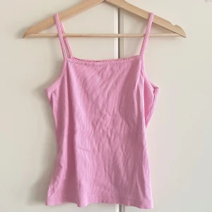 Ljusrosa ribbad linnetopp - Söt ljusrosa linnetopp med smala axelband och ribbad struktur. Toppen är ärmlös och har en enkel, rak passform som passar perfekt till sommaren. Materialet känns mjukt och stretchigt, vilket gör den superbekväm att bära.