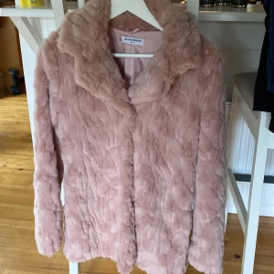 Rosa pälsjacka från Glamorous - Supermjuk och fluffig rosa pälsjacka från Glamorous. Jackan har en klassisk krage, helrosa foder och stängs med knappar framtill. Perfekt för dig som vill sticka ut och hålla dig varm med stil. Passar dig som gillar en trendig och cozy vibe.