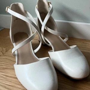 Vita Högklackade Skor med Spänne - Säljer dessa vita högklackade skor. De har en 4 cm klack och stängs med guldspänne på sidan. De är i väldigt fint skick eftersom att de endast använts en gång.