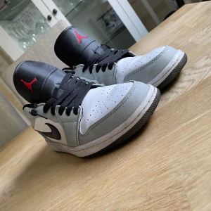 Nike Air Jordan 1 Low smokey grey - Nike Air Jordan 1 Low i grått och vitt skinn med svarta detaljer och svart swoosh. Tungan är svart med röd Jumpman-logga och hälen har broderad Air Jordan-logga i rött. Klassisk siluett med svart snörning och perforerad tå för extra stil. Pris kan diskuteras:)
