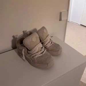 Beige chunky sneakers med grova snören - Säljer ett par beige chunky sneakers med riktigt grova snören och meshdetaljer. Skorna har en kraftig sula och coola paneler i mocka och textil. Perfekta för dig som gillar statement-skor och vill sticka ut med din stil.