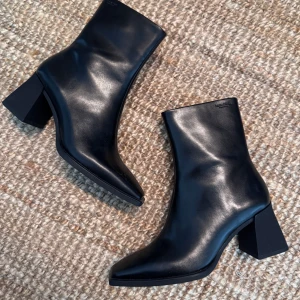 Vagabond Hedda - Snygga svarta stövletter från Vagabond i slätt skinn. Modellen har fyrkantig tå, blockklack och dragkedja på insidan. Perfekta för dig som gillar minimalistisk och stilren look med en modern twist. Köpta för 1700kr hos Vagabond. Helt nya och oanvända. Samma skick som i butik. 