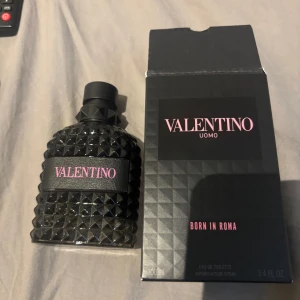 Valentino Uomo Born In Roma EdT 100ml - Snygg parfymflaska från Valentino Uomo Born In Roma, 100ml Eau de Toilette. Flaskan är svart med coola nitar och rosa text, och har en lyxig, edgy design. Kommer med originalkartong i matchande svart med rosa detaljer. Perfekt för dig som gillar exklusiva dofter och stil.