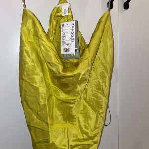Gul satin klänning från H&M - Säljer en snygg gul klänning från H&M i glansigt satinmaterial. Klänningen har en kort längd och smala axelband, perfekt för dig som vill sticka ut med en färgstark look. Passformen är normal och tyget har en lyxig känsla.