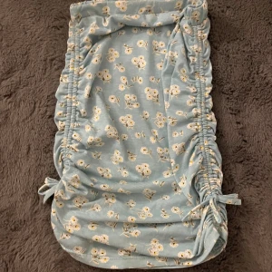 Blommig ljusblå kortklänning med snörning - Supersöt ljusblå kortklänning med vita och gula blommor. Klänningen har snörning på sidorna som ger en snygg rynkad effekt och kan justeras för att passa perfekt. Mjuk och skön bomull, perfekt för varma dagar. Fräsch och ungdomlig stil!