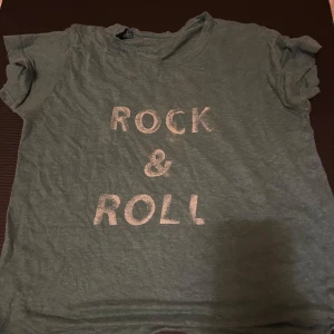 Grön t-shirt med Rock & Roll-tryck - Cool grön t-shirt med texten 'ROCK & ROLL' i vitt framtill. Klassisk rund hals och korta ärmar. Perfekt för dig som gillar musik och vill ha en avslappnad stil. Materialet känns mjukt och lätt, troligtvis bomull eller polyester.