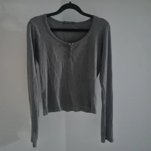 Grå långärmad topp Brandy Melville - Grå långärmad topp från Brandy Melville med rund halsringning och tre knappar framtill. Tunn och mjuk i bomullsmaterial, perfekt för lager-på-lager. Enkel och stilren design som funkar till allt.