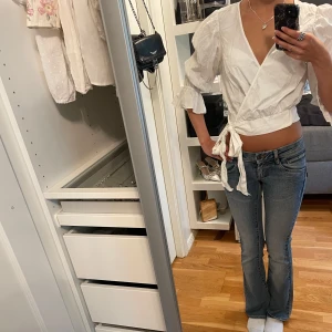 Vit omlottblus med puffärm - Vit omlottblus med puffiga trekvartsärmar, volang och v-ringning. Storlek 38, men knyts i sidan för en snygg passform, vilket gör att den passar storlek 34-38 (XS-M).