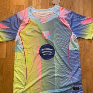 Nike x FC Barcelona pastell fotbollströja - Säljer en limited edition FC Barcelona fotbollströja från Nike med pastellfärger i blått, rosa, gult och grönt. Tröjan har korta ärmar, Dri-FIT material och coola linjer och prickar som mönster. Spotify-logga på bröstet och FCB-emblem i matchande färger.