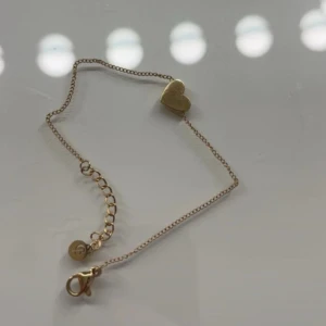Edblad armband - Fint armband i guld med en söt hjärtberlock. Tunn kedja och justerbar längd med karbinlås. Perfekt accessoar för att ge en romantisk touch till din stil. Helt oanvänd 