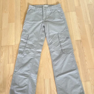 Grå cargobyxor  - Snygga grå cargobyxor från Gina Tricot i storlek 32 (Xxs). Jeans med raka ben och flera stora fickor på sidorna och bak. Byxorna har normal passform, bälteshällor och stängs med knapp och dragkedja. Inga defekter då dem inte är använda !!! Kontakta om du har några funderingar!!❤️