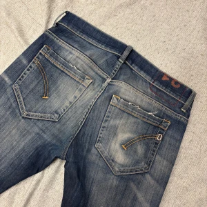 Dondup George - Snygga blå jeans från dondups med slitningar på knät och coola detaljer på bakfickorna. Jeansen har en klassisk femficksmodell, orangea sömmar och en något tvättad look. Perfekta för dig som gillar en avslappnad och trendig stil.