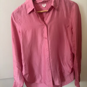 Rosa skjorta i silke  från Arket - Snygg rosa skjorta från Arket i 100% silke . Klassisk krage, knäppning framtill och långa ärmar. Skjortan har en stilren look och passar perfekt till jeans eller kjol. Enkel och tidlös design som är lätt att matcha. Det finns en liten defekt syns på sista bilden annars i superfint skick! 