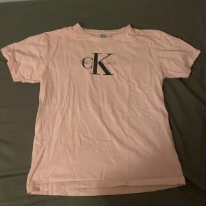 Ljusrosa Calvin Klein t-shirt - Snygg ljusrosa t-shirt från Calvin Klein med stor svart CK-logga på bröstet. Klassisk rund hals och korta ärmar, perfekt för en chill och stilren look. Tillverkad i mjuk bomull som känns skön mot huden. Passar dig som gillar enkel och trendig design. Jag tror dock inte att den e ekta men jag vet inte🩷