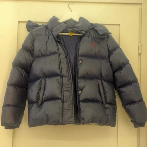 Blå dunjacka Polo Ralph Lauren  - Snygg mörkblå dunjacka från Polo Ralph Lauren med röd logo. Jackan har huva med dragkedja. Barnstorlek XL (16) passar till xs- s.💙 Perfekt för kalla dagar och riktigt skön att bära. Priset kan diskuteras!
