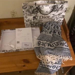 Blåvit halsduk från Dior - Exklusiv halsduk från Dior i blått och vitt med tydlig logotyp och mönster. Halsduken har fransar i ändarna och känns både lyxig och trendig. Perfekt accessoar för att lyfta din outfit med en touch av designerstil.
