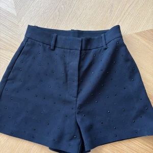 Svarta shorts med pärldetaljer - Snygga svarta shorts med små svarta pärlor över hela tyget. Klassisk passform med hällor för bälte och två fuskfickor bak. Perfekta för dig som vill ha något stilrent men ändå med en twist. Materialet känns stabilt och de är midwaist men kan ha low waist om man vill. Änvända ändats en gång❣️orginalpris 350kr