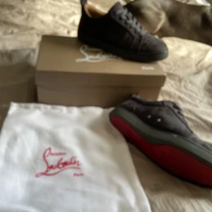 Christian Louboutin gråa mocka - Snygga gråa sneakers från Christian Louboutin i mocka med klassisk röd sula. Skorna har rund tå och diskreta detaljer. Perfekta för dig som vill ha en lyxig och stilren look med en ikonisk touch.