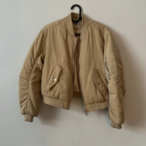 Beige bomberjacka från Zara, stl 152 - Snygg beige bomberjacka från Zara i storlek 152. Jackan har klassisk bombermodell med ribbade muddar, dragkedja framtill och fickor med lock. Ärmen har en cool detalj med dragkedja. Perfekt för dig som vill ha en stilren och trendig look.