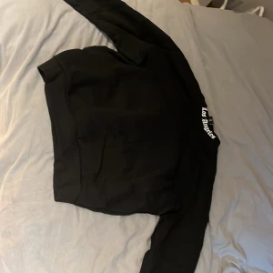 Svart oversized sweatshirt Los Angeles - Svart oversized sweatshirt från Black Squad med stor vit text 'Los Angeles' över ryggen. Tröjan har långa ärmar, ribbade muddar och är tillverkad i mjuk bomullsmix. Perfekt för en chill streetwear-look.