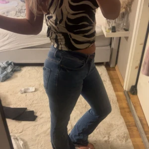 Blå bootcut jeans med hög midja - Säljer ett par snygga blå jeans med bootcut passform och hög midja. Jeansen har klassiska fem fickor och en mörkblå tvätt som passar till allt. Materialet är jeans och de sitter riktigt bra över höften och låren. Perfekt för dig som gillar en tidlös stil.