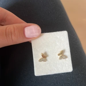 Guldiga örhängen med glittriga detaljer - Säljer ett par små örhängen i guldton med söt fjärilsform. Den nedre delen är täckt av glittrande stenar som ger extra bling.