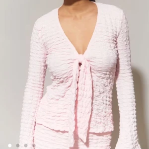 Ljusrosa topp från Gina Tricot - Supersöt ljusrosa topp från Gina Tricot med lång ärm och knyt framtill. Toppen har strukturerat material och v-ringning🩷Nypris 329kr