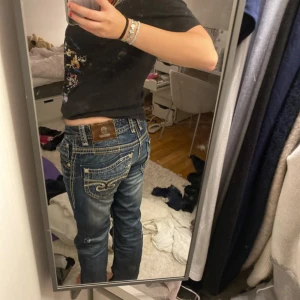 Blå Miss Me liknande jeans med broderade fickor - Säljer ett par blå jeans från blue Monkey med snygga broderade detaljer på bakfickorna och slitningar framtill. Jeansen har låg midja, raka ben och kontrastsömmar som ger en cool look. Perfekt för dig som gillar statement-jeans med mycket detaljer.