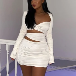 Vit omlott kortklänning med snörning - Supersnygg vit kortklänning med omlott-design och långärmade ärmar. Klänningen har snörning runt midjan och är figurnära med rynkade detaljer som ger en cool look. Perfekt för dig som gillar trendiga och stilrena outfits.