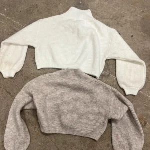 Två croppade stickade tröjor i vitt och grått - Säljer två croppade stickade tröjor, en i vitt och en i ljusgrått. Båda har lång ärm, hög krage och ribbad struktur. Perfekta att styla För jeans eller kjol för trendig look. Denna tröja har ingen storlek Men det är 140/146! Kolla bild 2 för de deffekten som finns. ✨