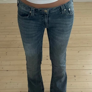True Religion blå bootcut jeans med rosa sömmar - Säljer ett par slutsålda blå jeans från True Religion med ikoniska bakfickor och snygga kontrastsömmar. Jeansen har bootcut-modell och klassisk femficksdesign. Materialet är jeans med en lätt tvättad look och låg midja. Perfekta för dig som gillar streetstyle och vill sticka ut. Lägre pris då dem är uppsydda, jag är 164/165 å är perfekta i längden. Kan gå ner i pris 