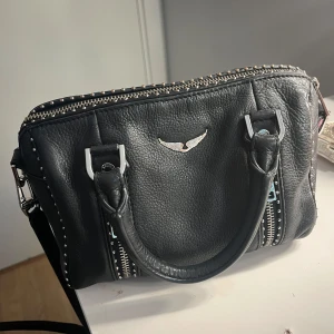  Zadig & Voltaire väska - Säljer min Zadig sunny bag i storlek xs. Köpte den i butiken för ca 2 år sedan men den är sparsamt använd och i mycket fint skick. Den har inga slitningar förutom att några av nitarna blivit lite missfärgade (inget som syns om man inte kollar nära!). Dustbag ingår, säljer för 2500kr💕