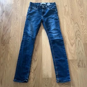 Levi's 510 skinny jeans blå - Säljer ett par Levi's 510 skinny jeans i klassisk blå denim. Jeansen har fem fickor, smal passform och snygga slitningar för en cool look. Perfekta för dig som gillar en tajtare stil och vill ha ett par jeans som funkar till allt.