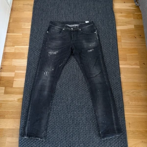 Svarta Dondup George jeans - Svarta skinny jeans från Dondup i modell george. Snygga slitna detaljer och små färgstänk. Använda ett fåtal gånger men fortfarande i nyskick! Storlek 33