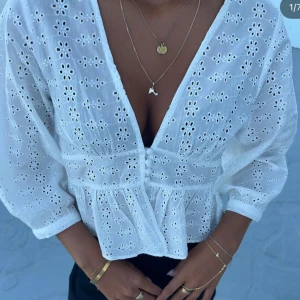 Vit blus med broderade blommor - Superfin vit blus med broderade blommor och v-ringning. Blusen har trekvartsärmar, knappar framtill och en lätt volang nedtill. Perfekt för dig som gillar romantiska detaljer och luftig bomull.