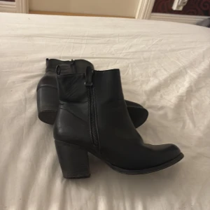 Svarta boots med klack och dragkedja - Säljer ett par svarta boots i skinn med chunky klack och dragkedja på sidan. Skorna har en rund tå och en stilren design som passar till många outfits. Perfekta för dig som gillar en klassisk look med lite edge.