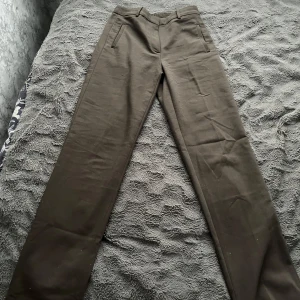 Brungröna kostymbyxor med raka ben - Jättesnygga olivgröna kostymbyxor med raka ben och klassisk passform. Byxorna har hällor för bälte, diskreta fickor fram och bak samt stängs med dragkedja och knapp. Perfekta för en clean och stilren look. Vid frågor hör av dig!