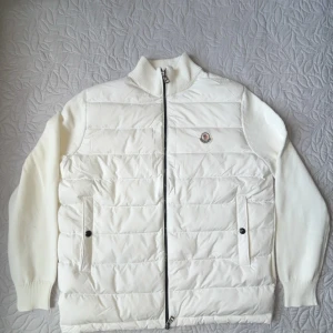 Moncler cardigan - Vit cardigan från Moncler med stickade ärmar och quiltad front. Jackan har dragkedja, ribbad krage och två fickor med knappstängning.