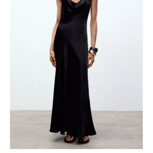 Svart långklänning i satin - Supersnygg svart långklänning med släpande siluett och lätt glansigt satintyg. Klänningen har ärmlös design och en snygg draperad urringning som ger en elegant vibe. Helt ny klänning från Zara, stolek s, lappen är kvar!💗