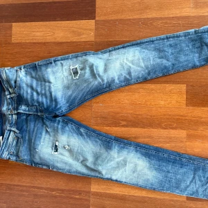 Slim fit Glenn blå jeans med slitningar - Snygga slim fit jeans från Jack&jones i en tvättad blå färg med coola slitningar och hål på framsidan. Klassisk femficksmodell med bruna sömmar och skinny passform. Modellen är Glenn. 