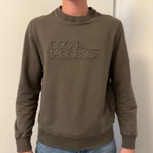  sweatshirt från Oscar Jacobson - Säljer en grön sweatshirt från Oscar Jacobson i storlek M. Tröjan har rund hals, ribbade muddar och ett broderat logotyptryck framtill. Skön och stilren modell i mjuk bomull, perfekt till jeans eller chinos.