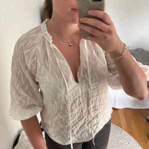 Vit blus med snörning och struktur - Säljer en luftig vit blus med snygg struktur och diskret mönster. Blusen har v-ringning, snörning vid halsen och trekvartsärmar. Perfekt för dig som gillar en avslappnad men ändå trendig stil.