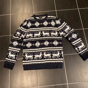 Mörkblå jultröja med mönster BoohooMAN - Säljer en mörkblå och vit stickad jultröja från BoohooMAN i storlek S. Tröjan har klassiskt vintermönster med snöflingor och renar, rund hals och långa ärmar. Perfekt för att maxa julkänslan med stil! I nyskick!