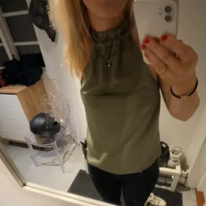 Halterneck topp - Snygg olivgrön ärmlös topp med hög hals och knytning i nacken. Lite nopprig kan skicka bättre bild privat 
