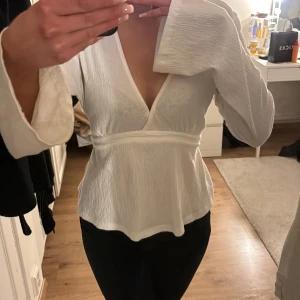 Vit blus med knytband - Säljer en stilren vit blus med långa ärmar och v-ringning. Blusen har ett knytband i ryggen som ger en fin passform. Perfekt för en elegant look.