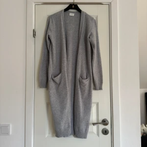 Grå lång kofta från Vila - Säljer en stilren och lång grå kofta från Vila. Den har långa ärmar och praktiska fickor framtill. Perfekt för kyliga dagar och att mysa i hemma. Passar till många olika outfits!