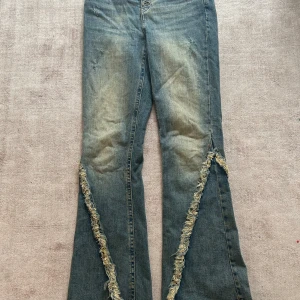 Blå jeans med slitna detaljer - Unika blå jeans med fransiga detaljer längs benen och vid midjan. De har en knappgylf och en vintage tvätt 