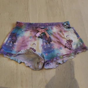 Färgglada shorts  - Säljer ett par färgglada shorts från Dolly Style med ett lekfullt mönster av enhörningar och hjärtan. Shortsen har en söt rosett framtill och volangdetaljer vid benen. Perfekta för den som älskar färg och mönster!