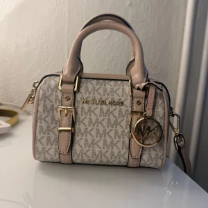 Mini Michael Kors väska - Intressekoll på min super söta beige/rosa handväska från Michael Kors! Väskan har guldfärgade detaljer och en avtagbar axelrem. Mycket bra skick, lite smått repig på dragkedjan men absolut inget man tänker på. Säljer direkt för 1500kr🥰