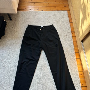 Svarta byxor från Filippa K - Snygga svarta byxor från Filippa K med en stilren design. Byxorna har en knapp och dragsko i midjan för extra komfort. Perfekta för en elegant och avslappnad look.